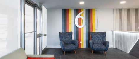 A modern waiting area with two armchairs, a red cushion, and a large number '6' on the wall.