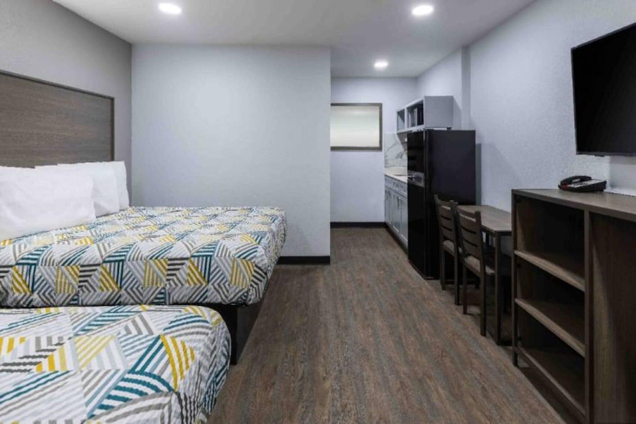 Quarto de hotel com duas camas, cozinha compacta, televisão e secretária com cadeiras.