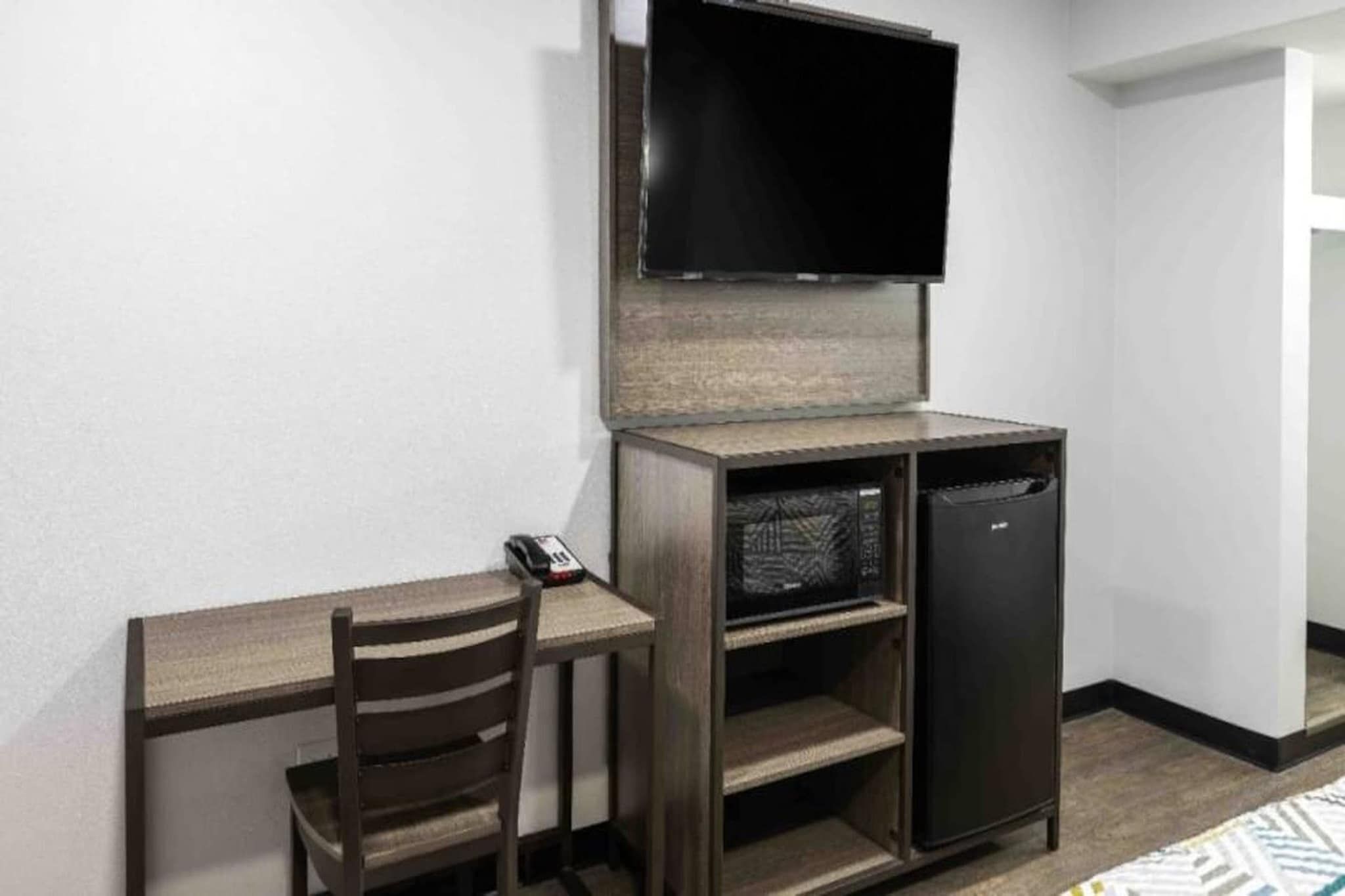 Quarto compacto com escrivaninha, cadeira e pequena geladeira.