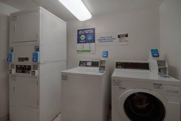 A laundry facility with multiple washing machines and dryers, a sign promoting laundry with an app, and a notice about item responsibility.