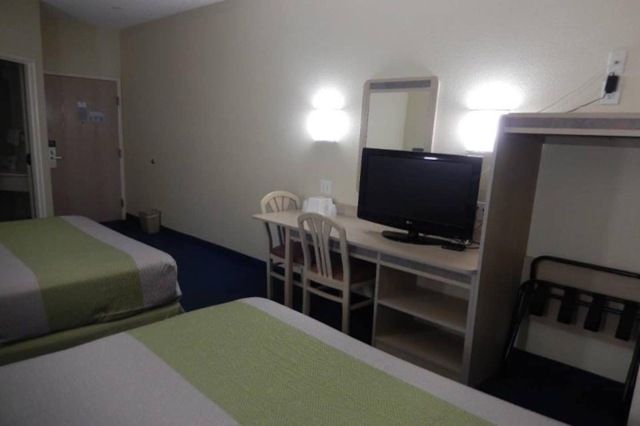 Quarto de hotel com duas camas, uma escrivaninha com televisão e uma cadeira.