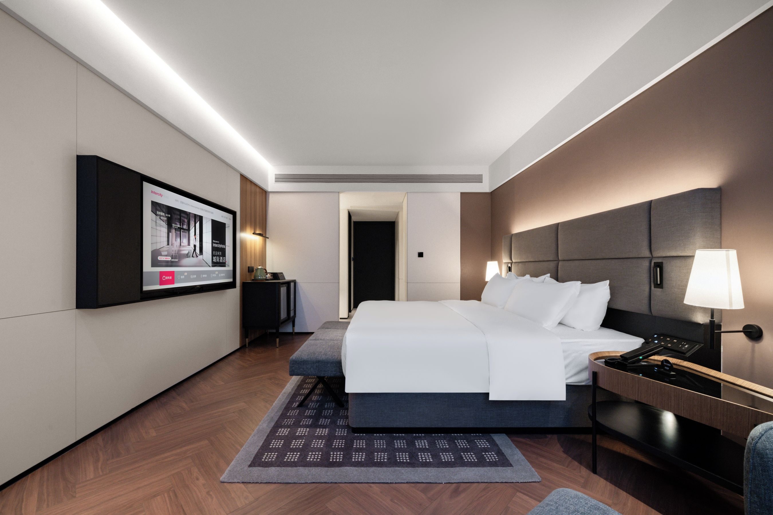 A modern hotel room with a large bed, bedside tables, a flat-screen TV, and a view of the hallway.