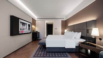 Quarto de hotel moderno com uma cama grande, mesas de cabeceira, uma TV de tela plana e vista para o corredor.
