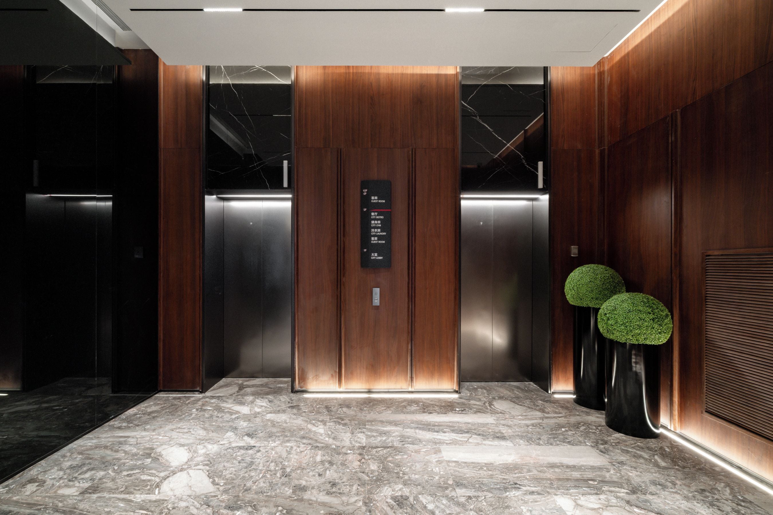 An elevator interior with a marble floor, wooden paneling, and a sign indicating room numbers.