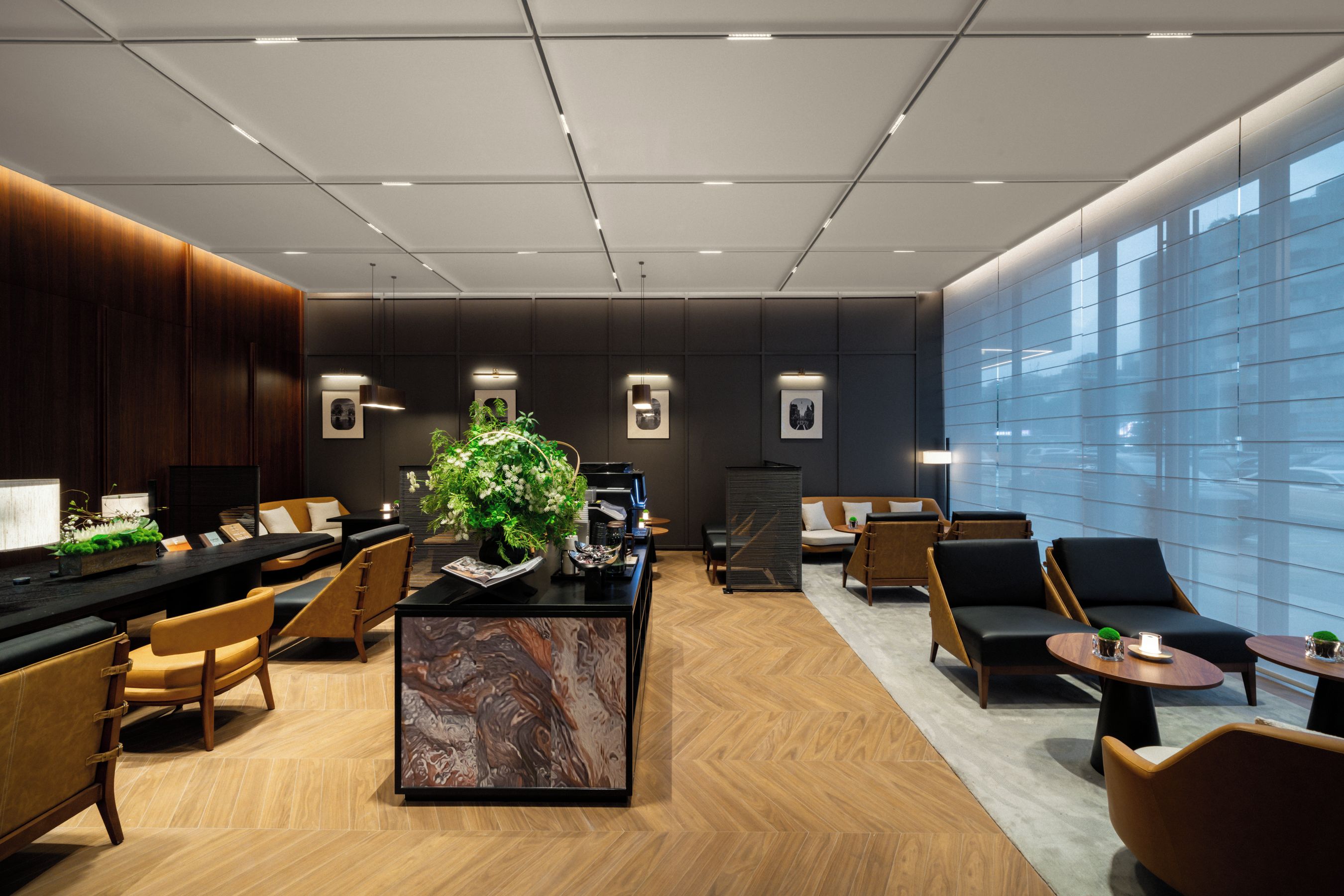 A modern hotel lobby with a reception desk, seating area, and large windows.