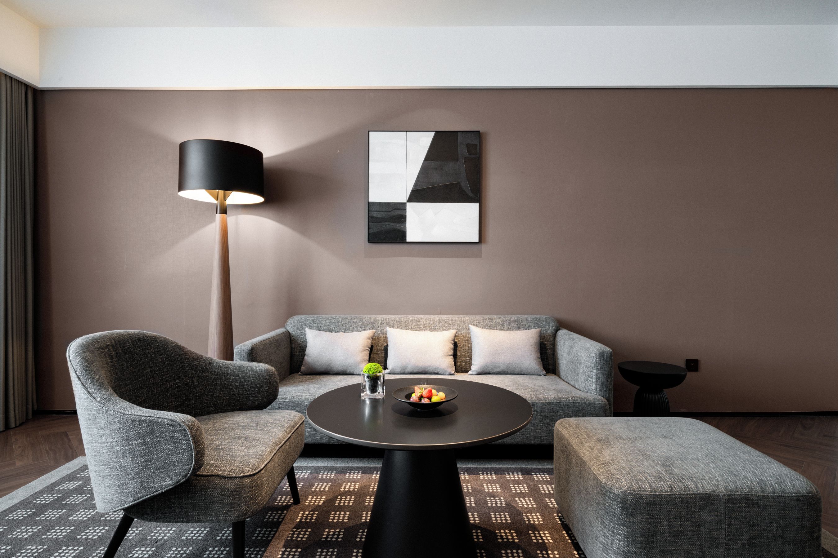 A modern living room with a sofa, armchair, and coffee table, a floor lamp, and a piece of abstract art on the wall.