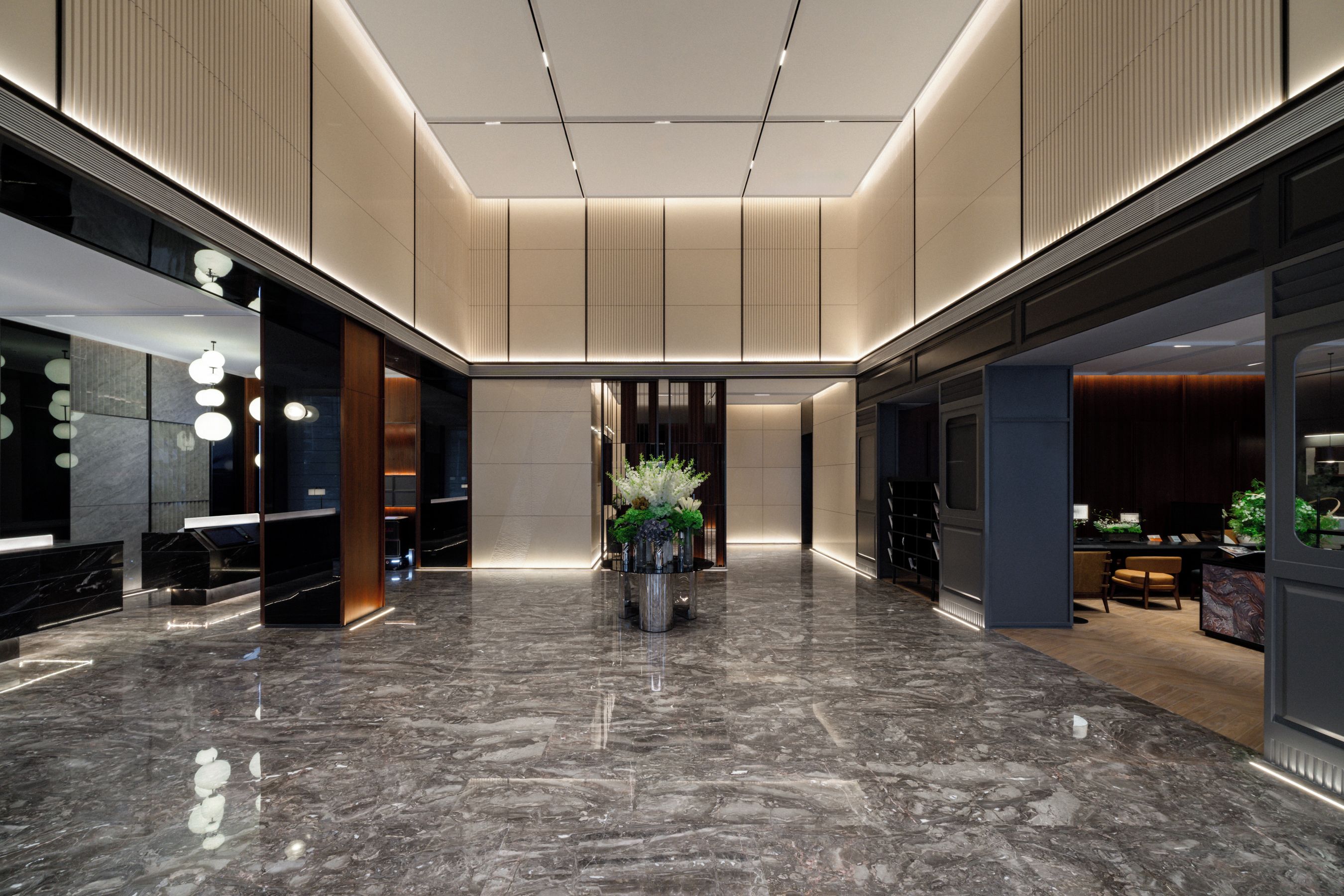 A modern lobby with a marble floor, recessed lighting, and a central plant arrangement.