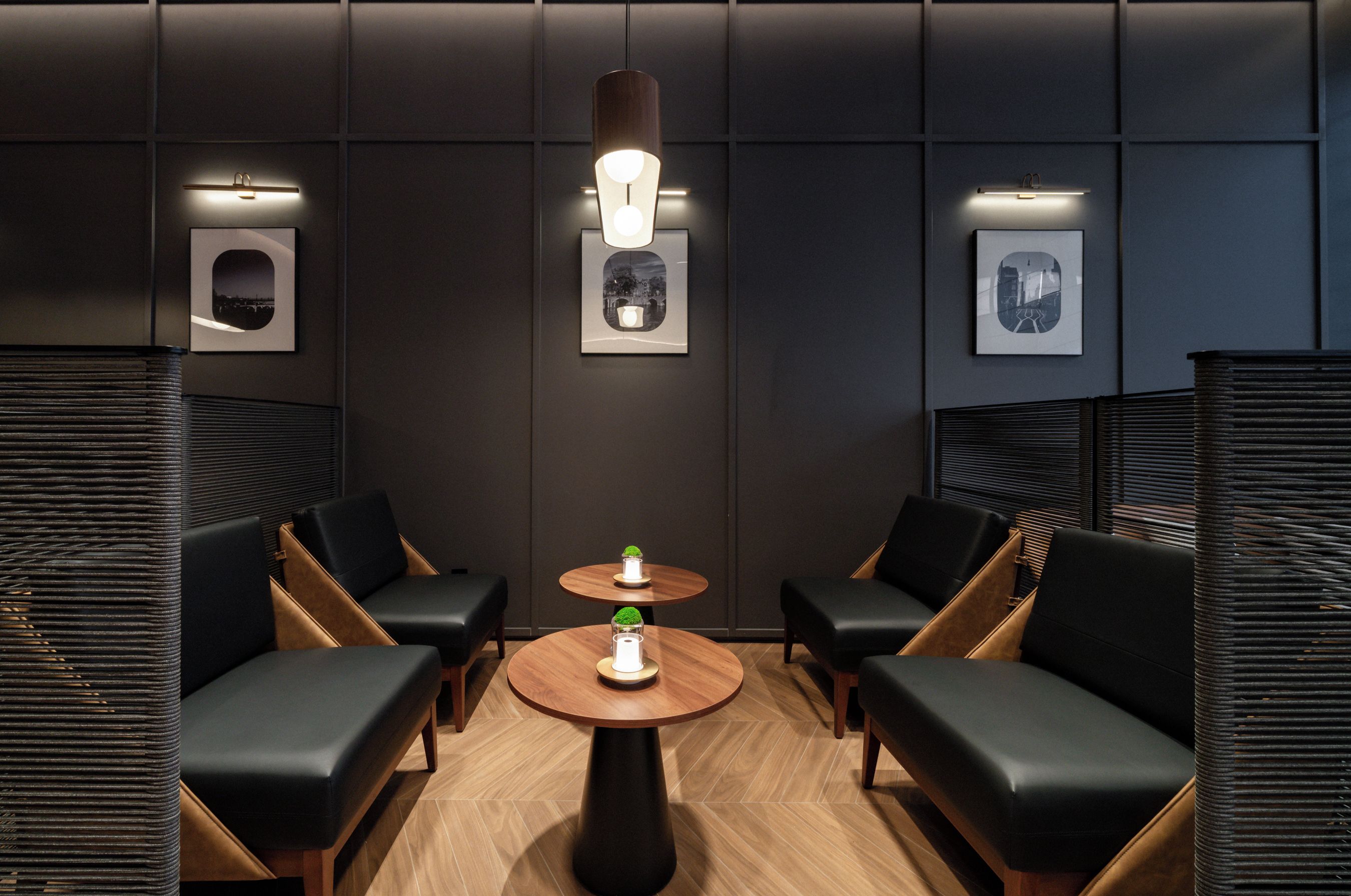 A modern lounge area with black leather chairs, a round wooden table, and framed artwork on the walls.