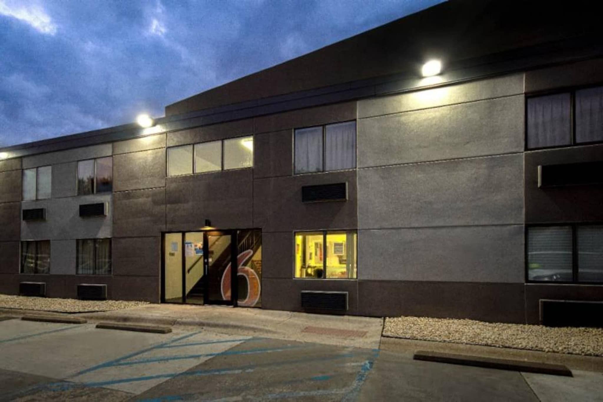 Un bâtiment moderne à la façade plate, doté de grandes fenêtres et d’un parking avec des places délimitées.