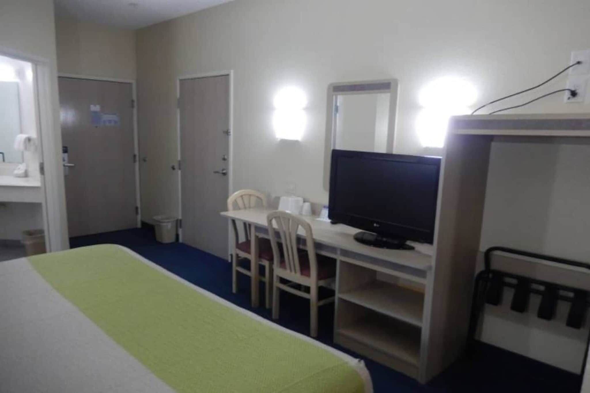 Ein Hotelzimmer mit einem Bett, einem Schreibtisch mit Stuhl, einem Fernseher und einem Spiegel.