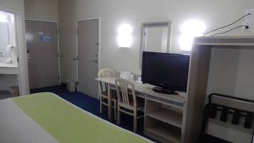 Una habitación de hotel con una cama, un escritorio con una silla, un televisor y un espejo.