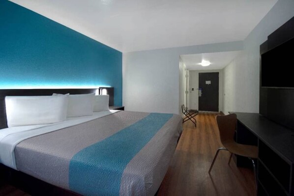 A hotel room with a large bed, a desk, a chair, and a television.
