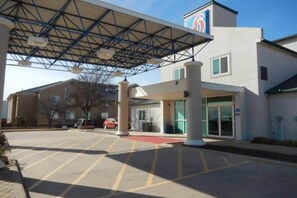 A hotel entrance with a covered parking area, a building with a '6' sign, and a clear sky. - 1 King Bed | Micfridge (MERRILLVILLE)