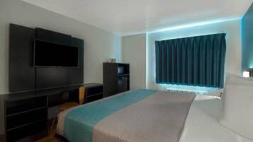 A modern bedroom with a large bed, a flat-screen TV mounted on the wall, a small cabinet, and a window with curtains.
