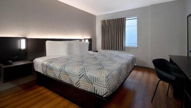 Habitación de hotel con una cama grande, un escritorio, una silla, una mesita de noche y un ventanal con cortinas.