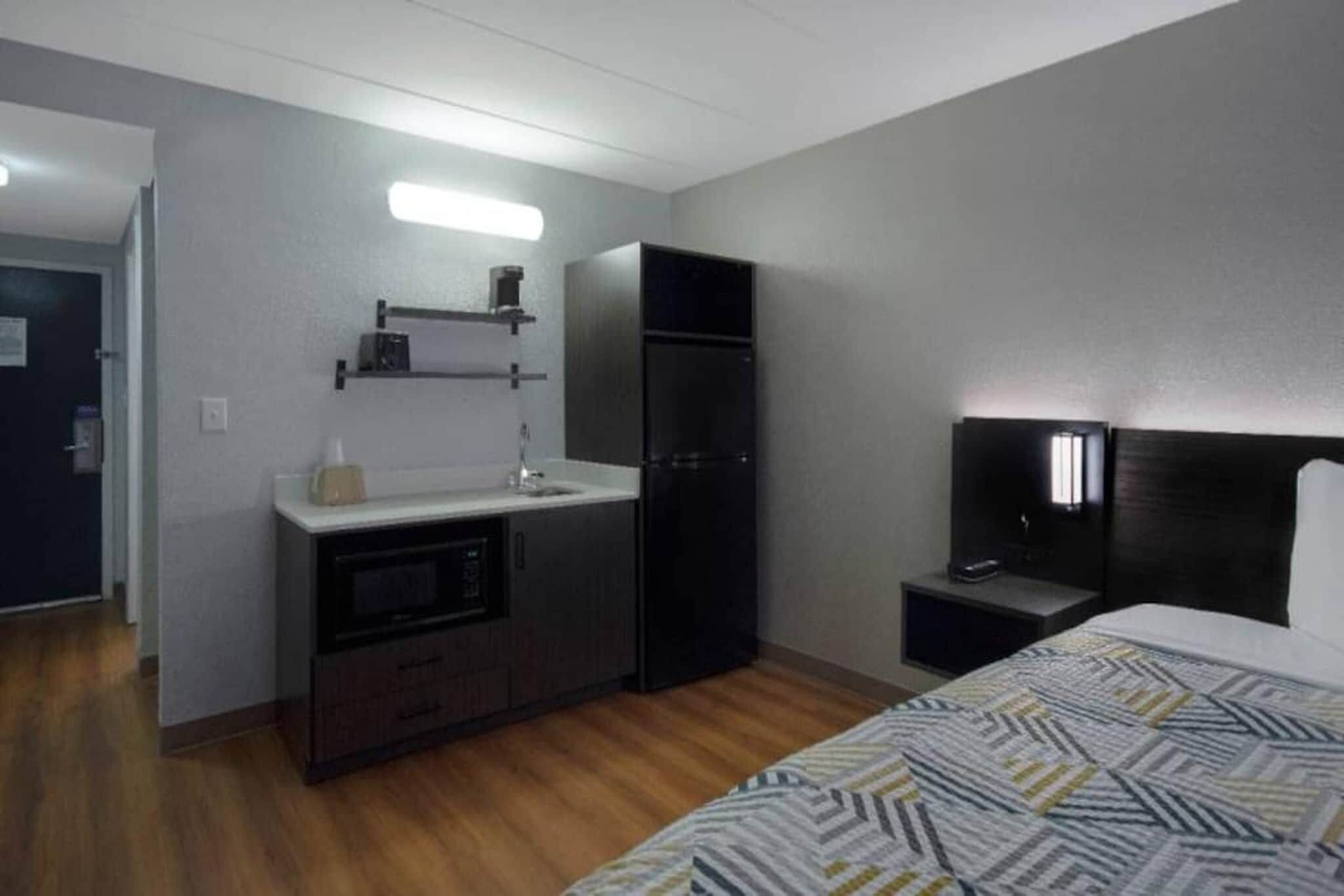 Ein kleines Hotelzimmer mit einer Küchenzeile, einem Bett, einem Nachttisch und einem Fernseher.
