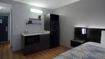 Ein kleines Hotelzimmer mit einer Küchenzeile, einem Bett, einem Nachttisch und einem Fernseher.