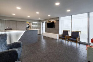 Un hall d’hôtel moderne avec un comptoir d’accueil, un espace salon et de grandes fenêtres.