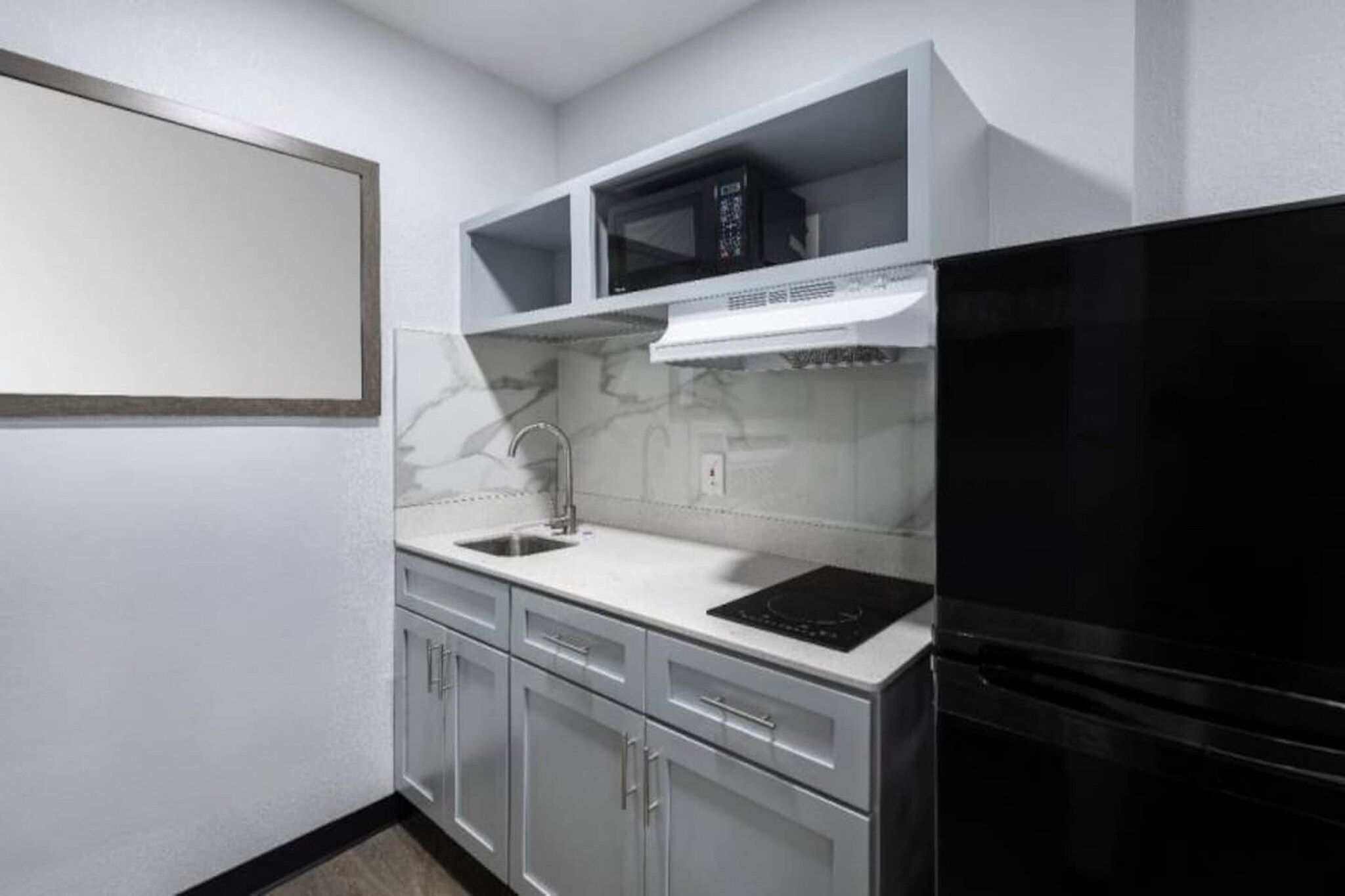 A compact kitchen with a black refrigerator, a microwave, and a stainless steel sink.
