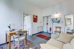 Uma sala de estar com sofá, mesa de jantar e cadeiras, tapete colorido e obras de arte nas paredes.