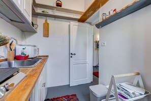 Cozinha compacta com bancada de madeira, porta branca e pequena lixeira.