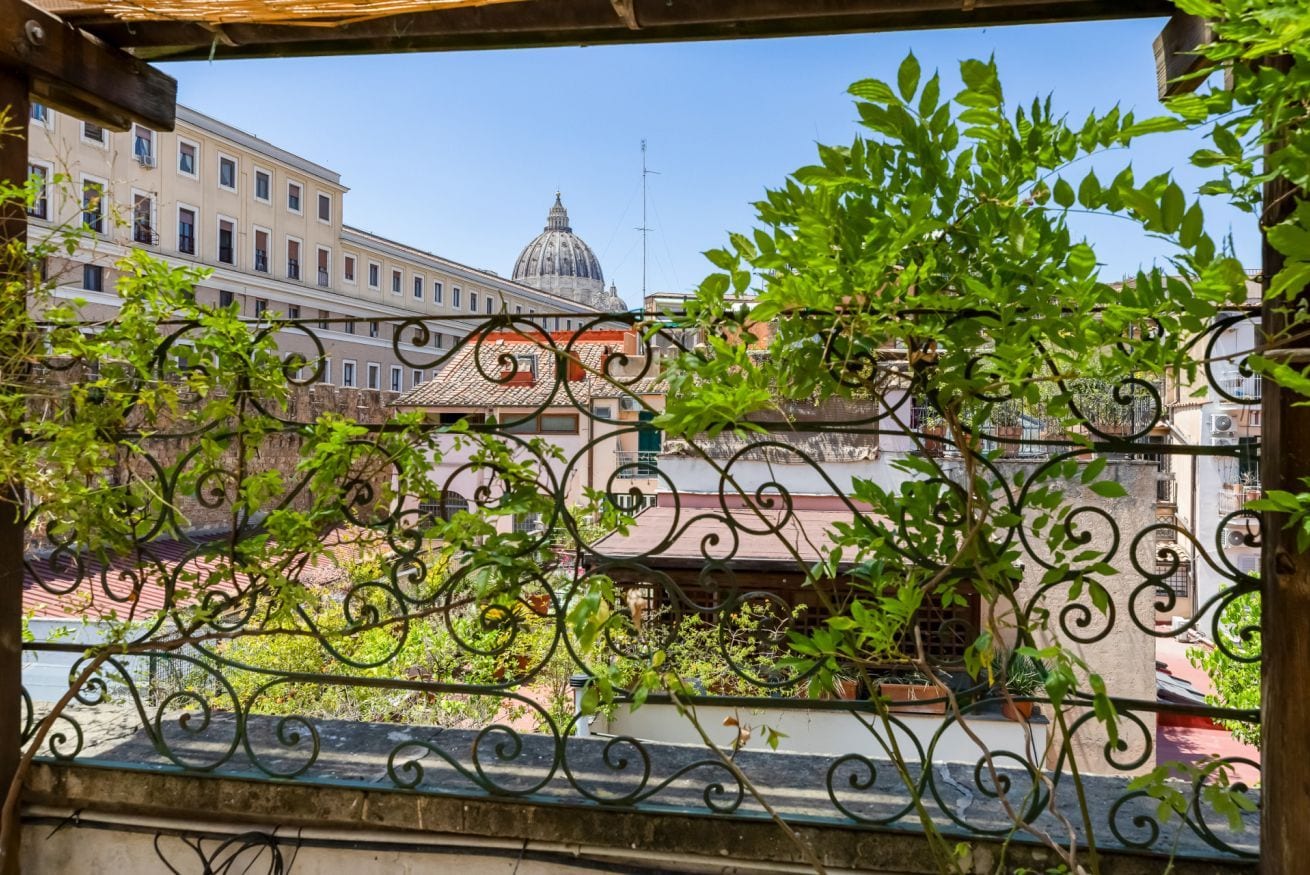 Un balcon orné de balustrades en fer forgé, une vue sur les immeubles et un ciel dégagé.
