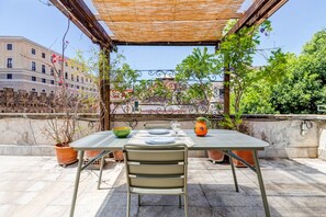 Ein Essbereich im Freien mit einem Tisch für zwei Personen, umgeben von Blumentöpfen und einer Pergola.