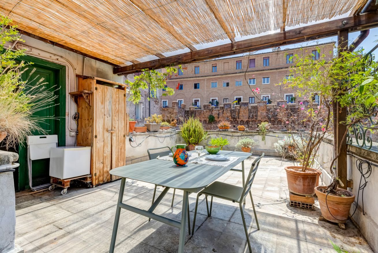 A patio with a table and chairs, surrounded by potted plants and a view of a building.