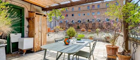 A patio with a table and chairs, surrounded by potted plants and a view of a building.
