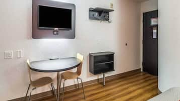 Ein kleiner Raum mit einem runden Tisch, zwei Stühlen, einem an der Wand befestigten Fernseher und einem kleinen Regal.