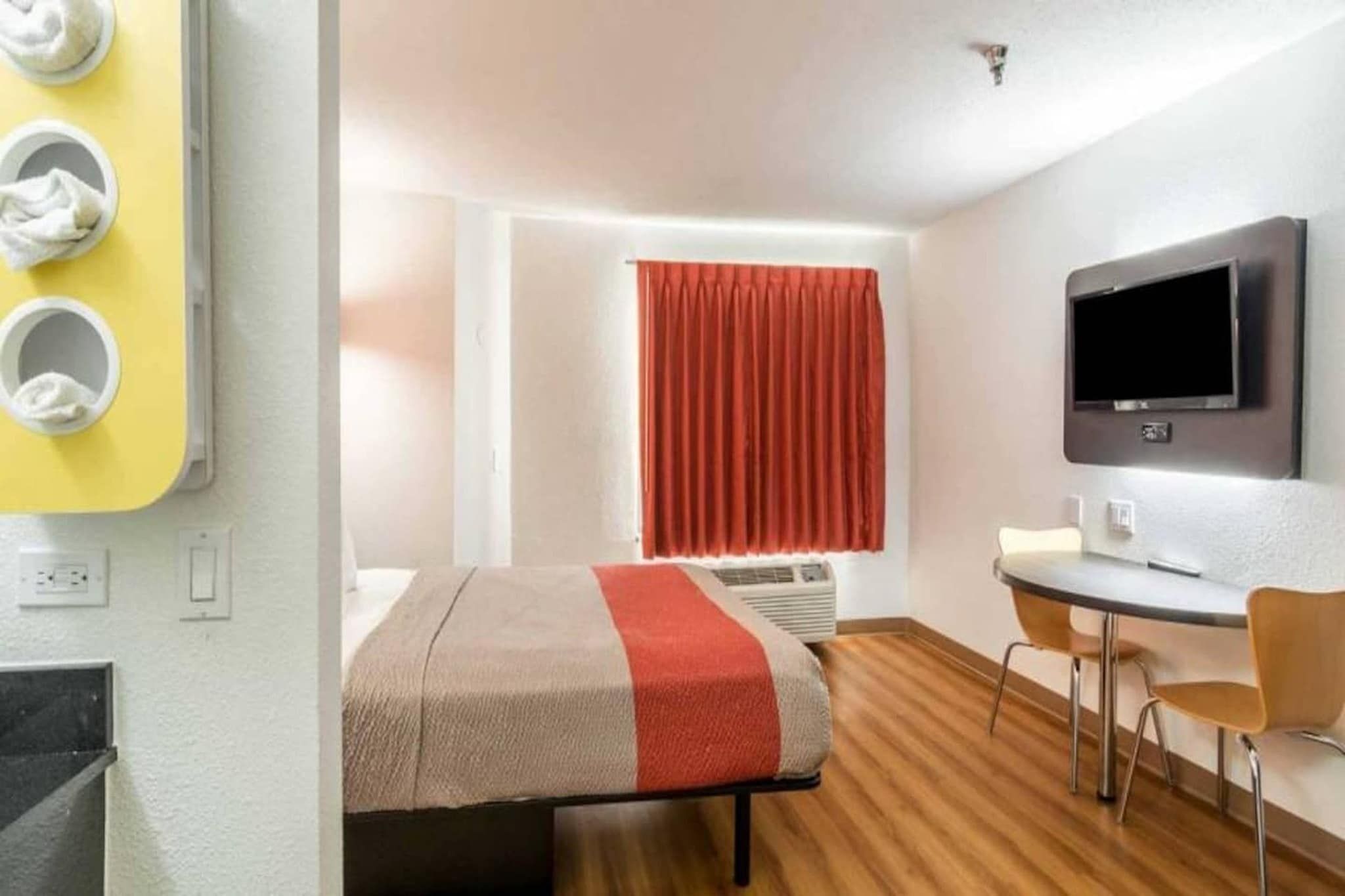 Une chambre d’hôtel équipée d’un lit, d’un bureau, d’une chaise, d’une télévision et d’une fenêtre avec des rideaux.