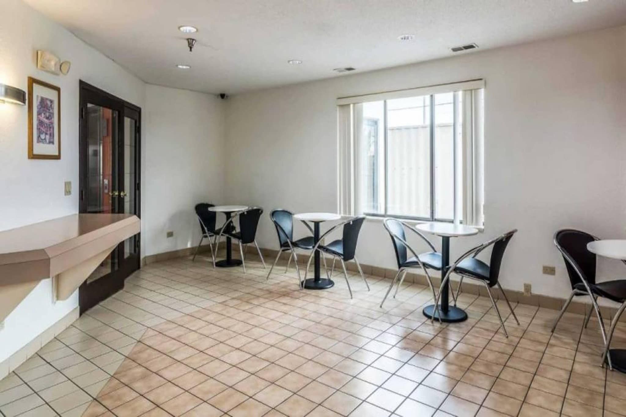 A room with a tiled floor, a counter, and four tables with chairs.