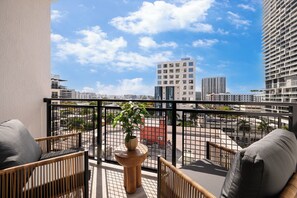 A balcony with wicker furniture, a potted plant, and a view of a cityscape with buildings. - #1 Hotel in Miami | Sleeps 12 | 2 Executive Suites w/ Rooftop Pool | Sense28 (Miami)