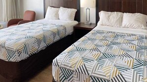 Hotellihuone, jossa on kaksi erillistä sänkyä, tuoli, yöpöytä ja lamppu.