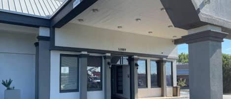 Een gebouw met een overdekte ingang, waarop 'LOBBY' staat, grote ramen en een kamerplant.
