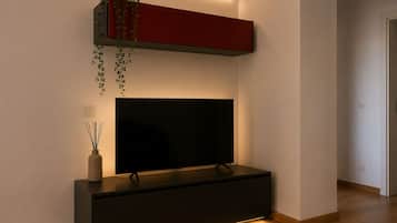 Una sala de estar moderna con un televisor de pantalla plana, piso de madera oscura y un mueble rojo con una planta colgante.