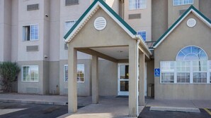 A building with a covered entrance, multiple windows, and a blue handicap accessibility sign. - Bright Queen Bed | Non-Smoking (Albuquerque NM)
