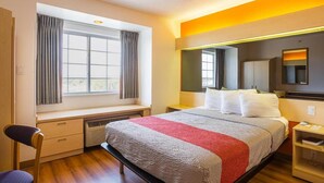 A hotel room with a bed, a desk, a chair, a window with curtains, and a bedside table. - Bright Queen Bed | Non-Smoking (Albuquerque NM)