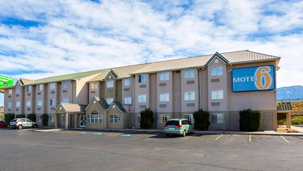 A motel with a sign indicating it is number 6. It has multiple floors with a flat roof and a parking lot in front. - Bright Queen Bed | Non-Smoking (Albuquerque NM)