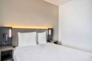 Een hotelkamer met een groot bed, twee nachtkastjes en een hoofdbord met ingebouwde verlichting.