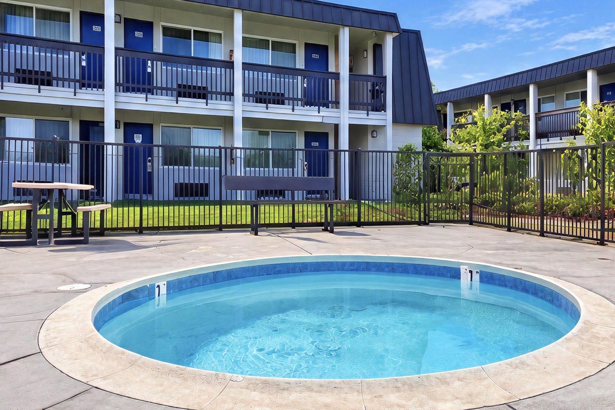 A swimming pool surrounded by a fenced area with a multi-story building in the background.
