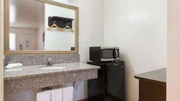 Een kleine badkamer met een wastafel van graniet, een spiegel, een zwarte koelkast en een magnetron.