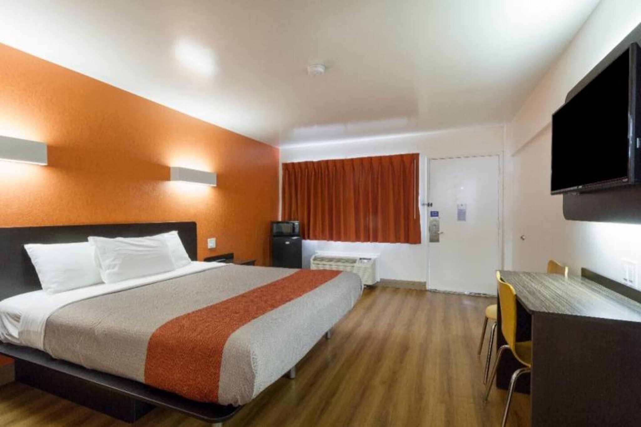A hotel room with a bed, a desk, a chair, a television, and a window with curtains.