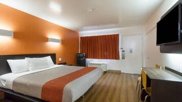 A hotel room with a bed, a desk, a chair, a television, and a window with curtains.