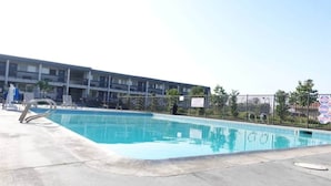 En swimmingpool med en metallstege, omgiven av ett staket, och en flervåningsbyggnad i bakgrunden.