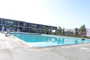 A swimming pool with a metal ladder, surrounded by a fence, and a multi-story building in the background. - 1 King Bed | Non-Smoking (Claremont)