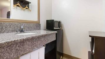 A bathroom with a granite countertop, a sink, a mirror, a towel rack, a microwave, and a cabinet.