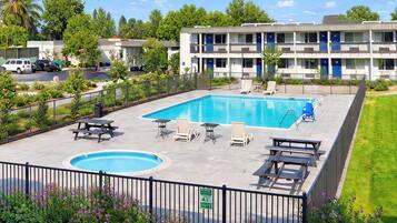 A swimming pool with lounge chairs and a picnic table, surrounded by a fence and greenery.