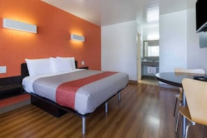 A hotel room with a bed, a desk, and a chair. There is a bathroom visible through an open door. - 1 King Bed | Non-Smoking (Claremont)