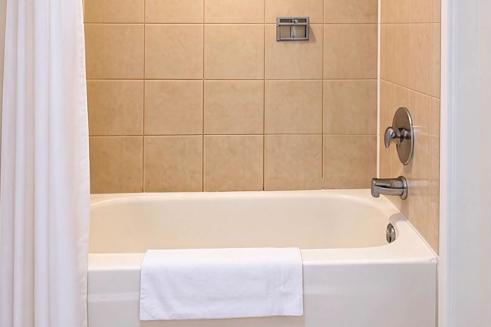 A bathroom with a bathtub, a towel, and beige tiles.